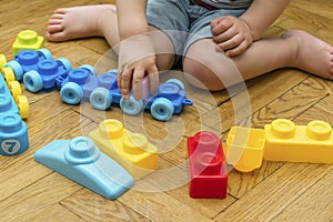 Cute little adorable caucasian boy playing with multi-colored constructor at home. Babys hands building tower of plastic