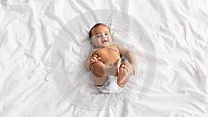 Cute little African American baby lying on bed at home