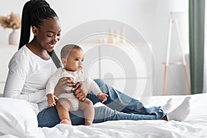 Cute little African American baby sitting on bed with mum