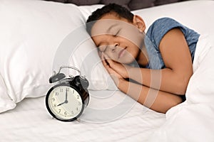 Cute little African-American boy with alarm clock sleeping