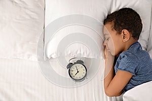 Cute little African-American boy with alarm clock sleeping