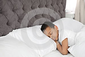 Cute little African-American boy sleeping in bed.