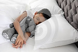 Cute little African-American boy with toy rabbit sleeping