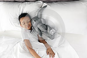 Cute little African-American boy with toy rabbit sleeping in bed