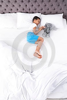 Cute little African-American boy with toy rabbit sleeping in bed, top view