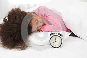 Cute little African-American girl with alarm clock sleeping