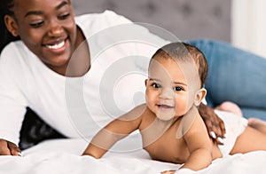 Cute little African American infant lying on bed with mom