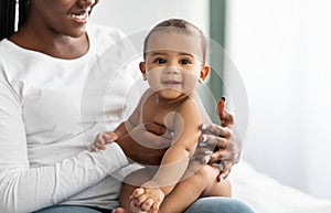 Cute little African American infant sitting on bed with mother