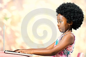 Cute little african girl with afro hairstyle typing on laptop.