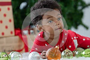 Cute little African kid boy in red clothes crawling and playing with Christmas tree decorated balls on floor