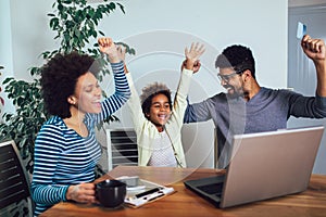 Little Afro-American girl and her beautiful young parents using a laptop and doing shopping online