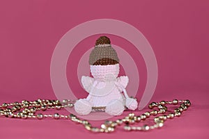 Cute little angel crocheted, handmade art. Amigurumi one white angel without face wears brown hat, sits on pink