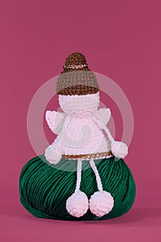 Cute little angel crocheted, handmade art. Amigurumi one white angel without face wears brown hat, sits on green ball of