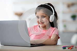 Cute Little Arab Girl In Wireless Headphones Having Online Lesson On Laptop