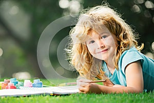 Cute little artist boy. Child boy draws in park laying in grass having fun on nature background.
