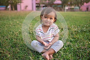 Cute little Asian 1 - 2 years old toddler baby girl child smiling at camera, barefoot practices yoga & meditating outdoors on