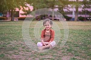 Cute little Asian 1 - 2 years old toddler baby girl child smiling at camera, barefoot practices yoga & meditating outdoors on