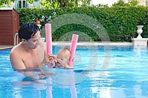 Cute little Asian 18 months / 1 year old toddler baby boy child learning to swim with pool noodle with dad at outdoor pool
