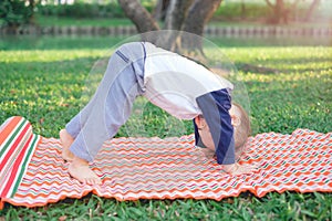 Cute little Asian 18 months / 1 year old toddler baby boy child practices yoga in Downward Facing Dog Pose and meditating outdoors