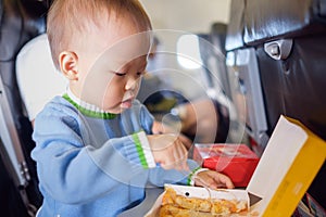 Cute little Asian 18 months / 1 year old toddler baby boy child wearing blue sweater eating food during flight on airplane