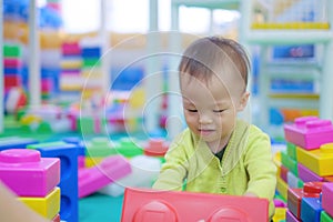 Cute little Asian 18 months / 1 year old toddler baby boy child wearing green sweater having fun playing with big colorful plastic