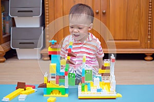 Cute little Asian 18 months / 1 year old toddler boy child having fun playing with colorful building blocks indoor in w-sitting po