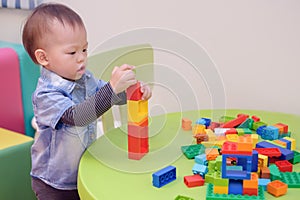 Cute little Asian 18 months / 1 year old toddler boy child having fun playing with colorful plastic blocks indoor at play school