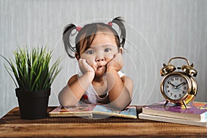 Cute little asian baby toddler making boring face while reading books with alarm clock