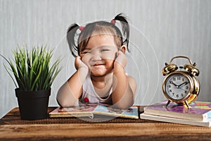 Cute little asian baby toddler making funny face or smiling while reading books with alarm clock