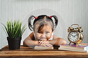 Cute little asian baby toddler making funny face or smiling while reading books with alarm clock