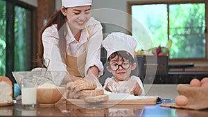 Cute little Asian boy and beautiful mother sifting dough flour in home kitchen on table for prepare to baking bakery and cake. Tha