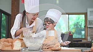 Cute little Asian boy and beautiful mother sifting dough flour with sifter sieve colander in home kitchen on table for prepare to