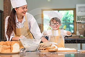 Cute little Asian boy and beautiful mother sifting dough flour with sifter sieve colander in home kitchen on table for prepare to