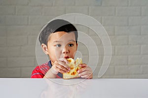 Cute little asian boy eating bread enjoying breakfast or snack on white table