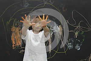 Cute little Asian boy enjoying arts and crafts painting with his hands on the blackboard