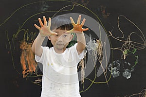 Cute little Asian boy enjoying arts and crafts painting with his hands on the blackboard