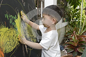 Cute little Asian boy enjoying arts and crafts painting with his hands on the blackboard