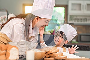 Cute little Asian boy painting beautiful woman face with dough flour. Chef team playing and baking bakery in home kitchen funny.