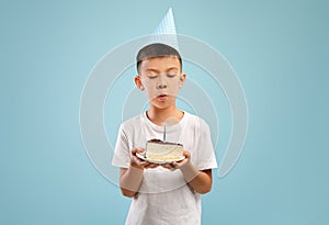 Cute Little Asian Boy In Party Hat Blowing Candle On Birthday Cake