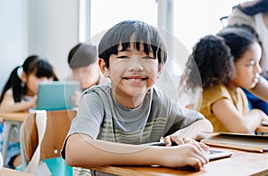 Cute little Asian boy smiling looking at camera and using laptop in computer class at the elementary school. Education, school,