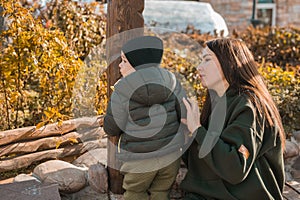 Cute little asian boy stands with mother outdoors copy space. Happy child walking in autumn park. Toddler baby boy wears