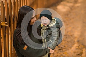Cute little asian boy stands with mother outdoors copy space. Happy child walking in autumn park. Toddler baby boy wears