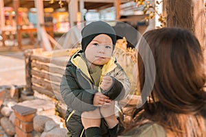 Cute little asian boy stands with mother outdoors. Happy child walking in autumn park. Toddler baby boy wears trendy