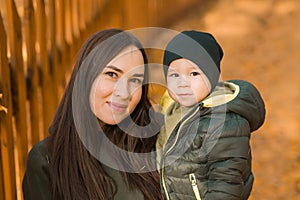 Cute little asian boy stands with mother outdoors. Happy child walking in autumn park. Toddler baby boy wears trendy