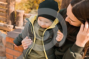 Cute little asian boy stands outdoors. Happy child walking in autumn park. Toddler baby boy wears trendy jacket and hat