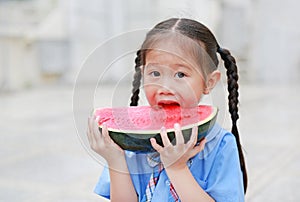 Cute little Asian child girl in school uniform enjoy eating fresh sliced watermelon