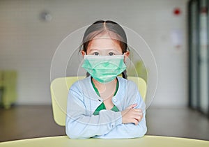 Cute little Asian child girl wearing a protective mask sitting on kid chair in children room