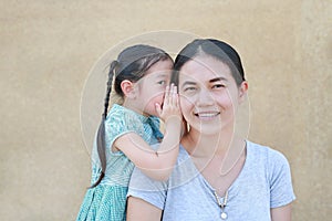 Cute little Asian child girl whispering a secret to her young mothers ear at home. Family and relationships concept