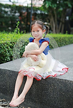 Cute little asian girl dressed with a fantasy outfit sitting in the garden with teddy bear