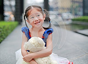 Cute little asian girl dressed with a fantasy outfit sitting in the garden with teddy bear